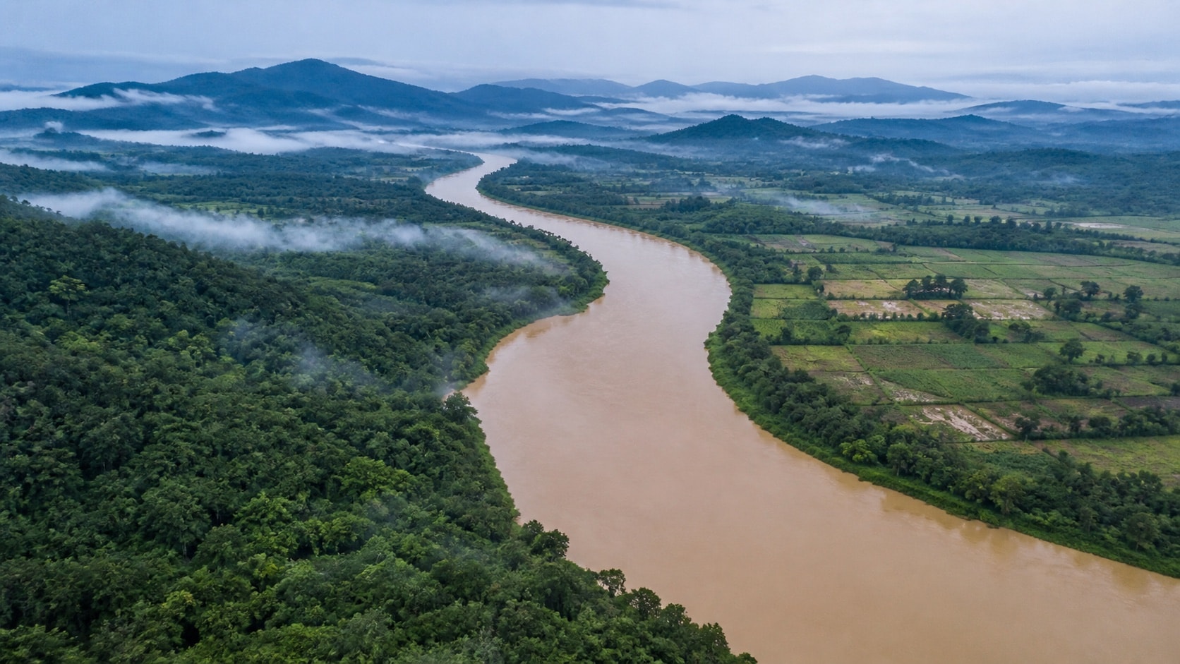 A broad river winding between forest canopy and small cultivated clearings